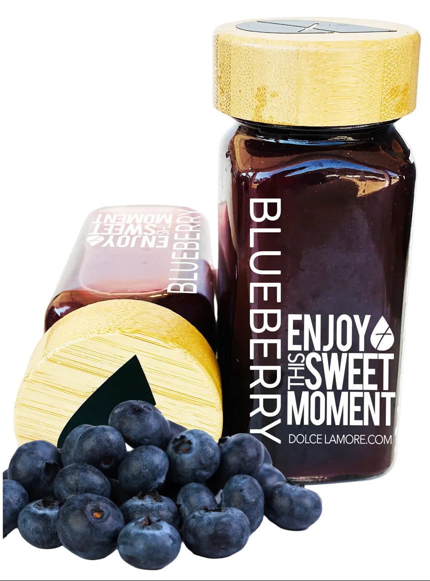 Jar of blueberry jam with a bamboo lid, surrounded by fresh blueberries on a white background.